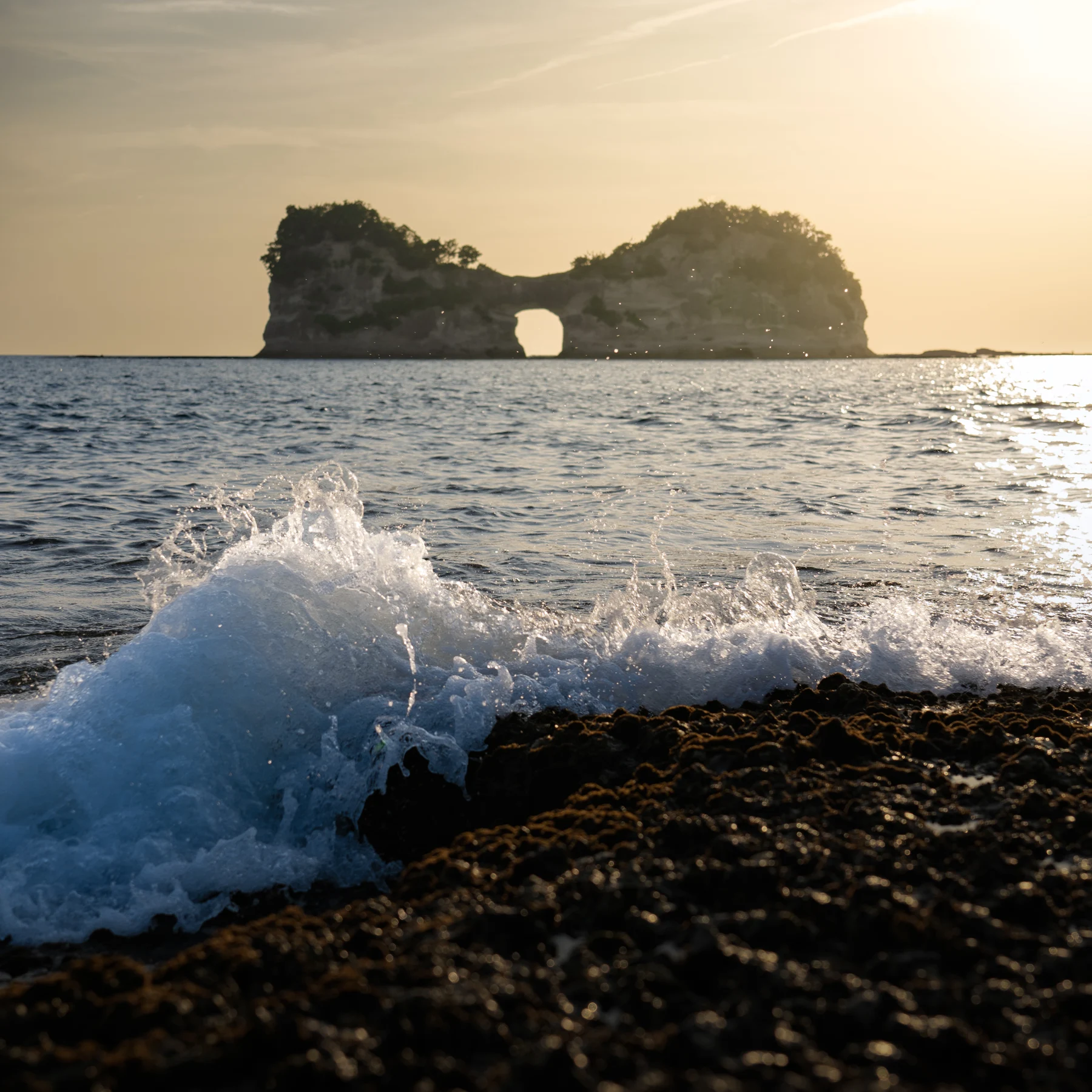 A breaking wave in front of an offshore rock arch.