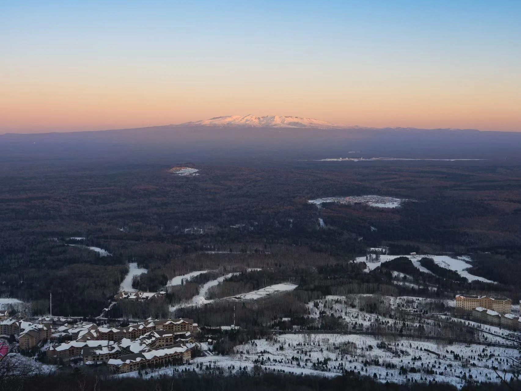 Snow-covered terrain beneath a pastel sunset.