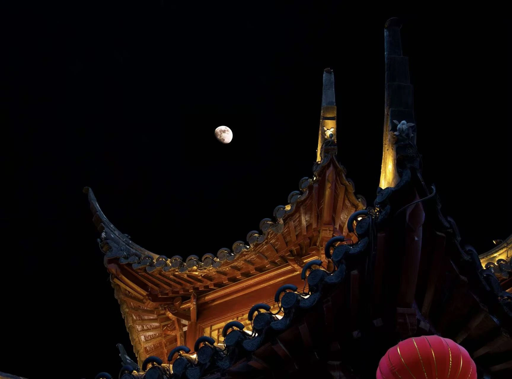 The moon above an illuminated traditional roof.