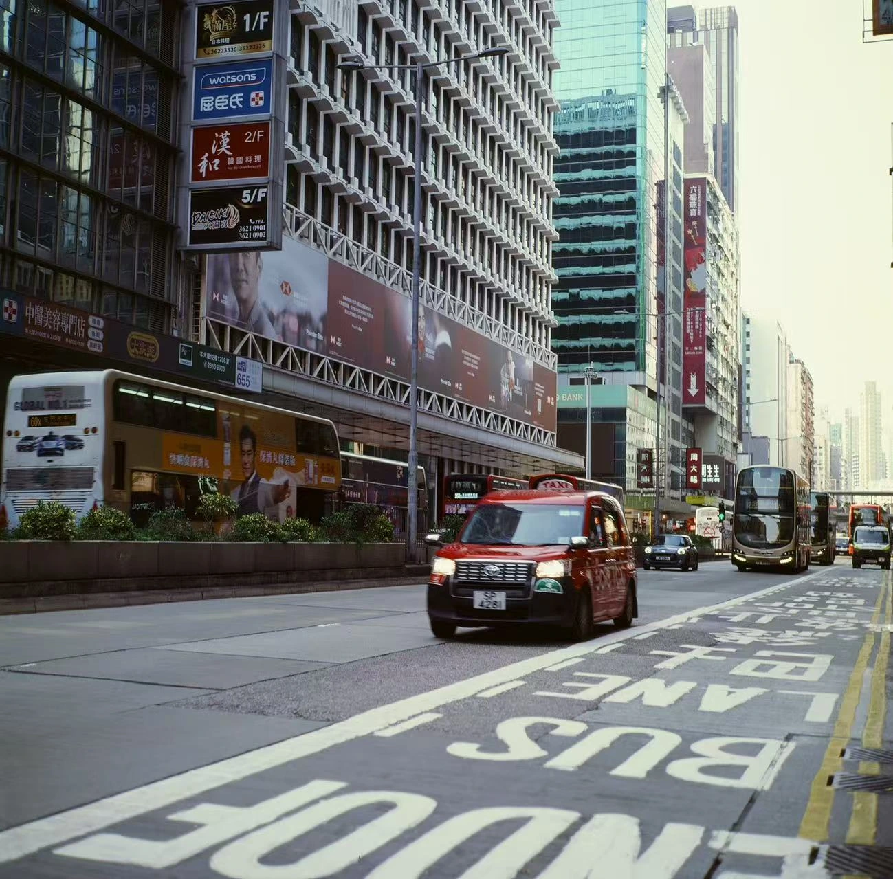 A red taxi among buildings and street markings.